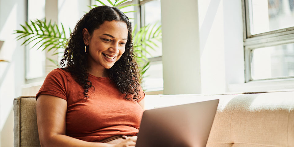 adult female sitting on a couch viewing data on a laptop